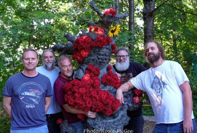 Five men posing with a tree sculpture decorated with many red roses in Central Oregon.