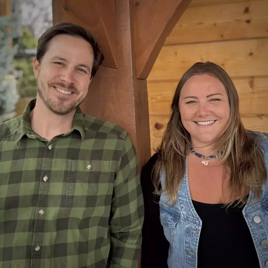 A smiling man and woman pose together in front of a wooden structure in Central Oregon.