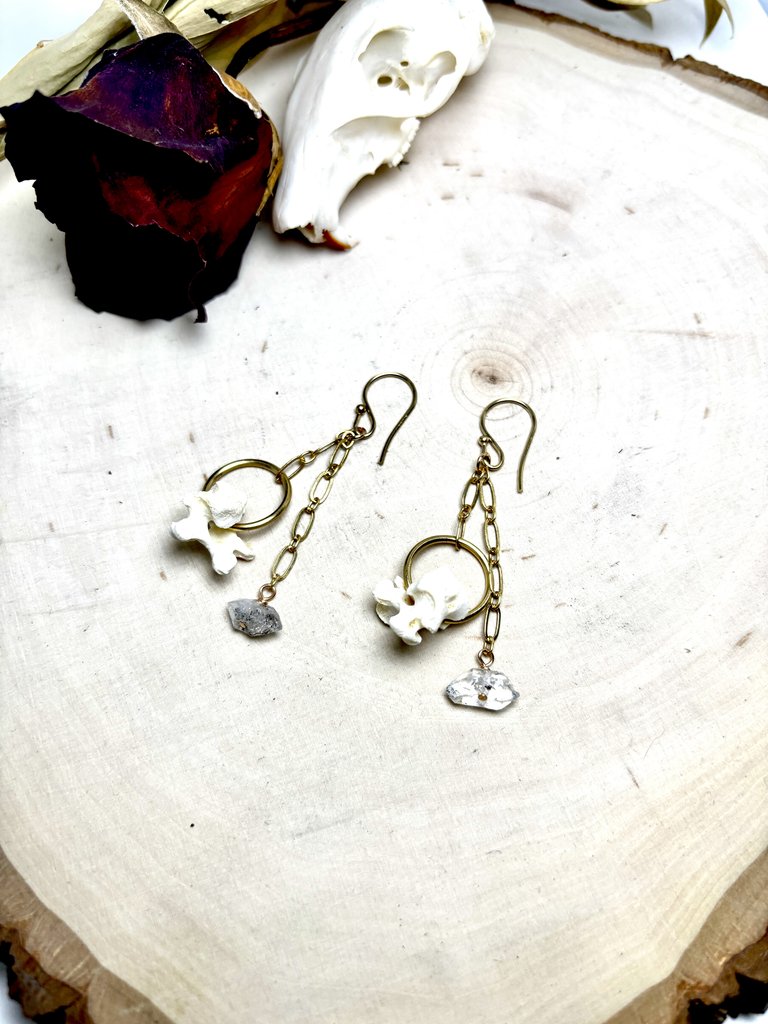 A pair of handmade earrings featuring small bones, gold chains, and raw crystals in Central Oregon.