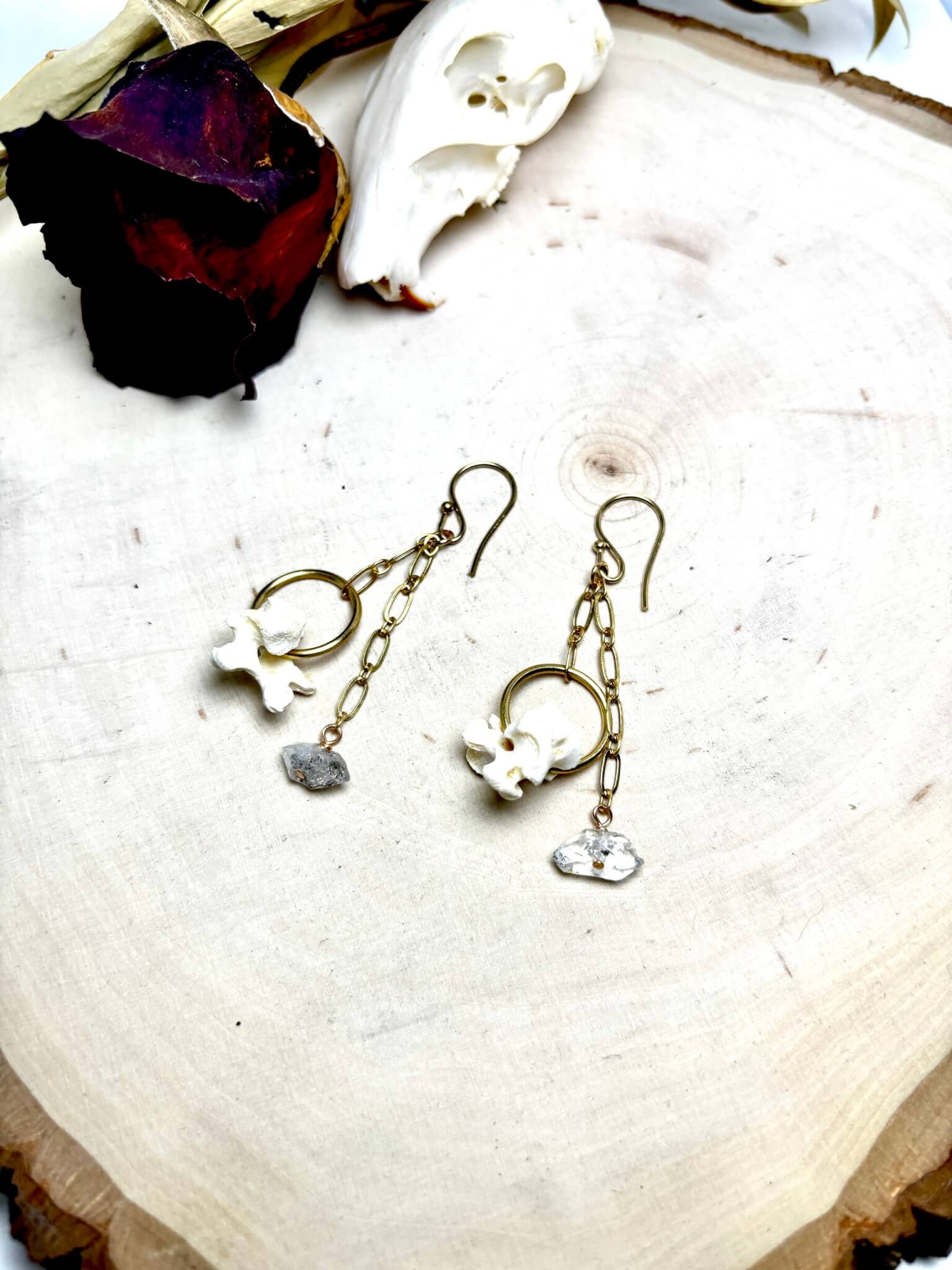 A pair of handmade earrings featuring small bones, gold chains, and raw crystals in Central Oregon.