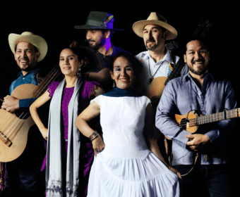 A group of five musicians posing together against a black background in Central Oregon.