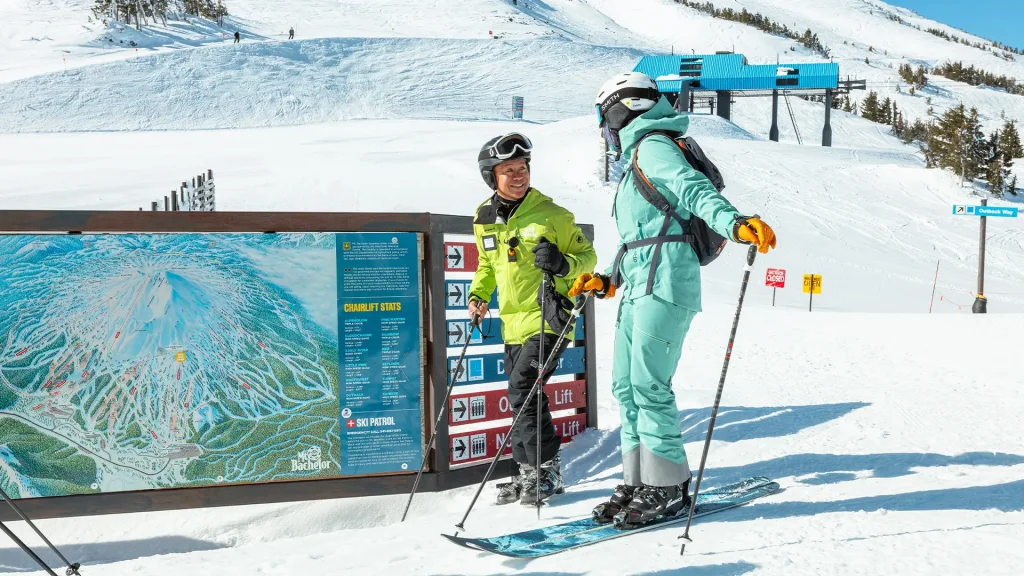 Two skiers in winter gear stand by a trail map at a ski resort in Central Oregon.