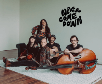 A five-piece folk band poses with their instruments in a studio in Central Oregon.