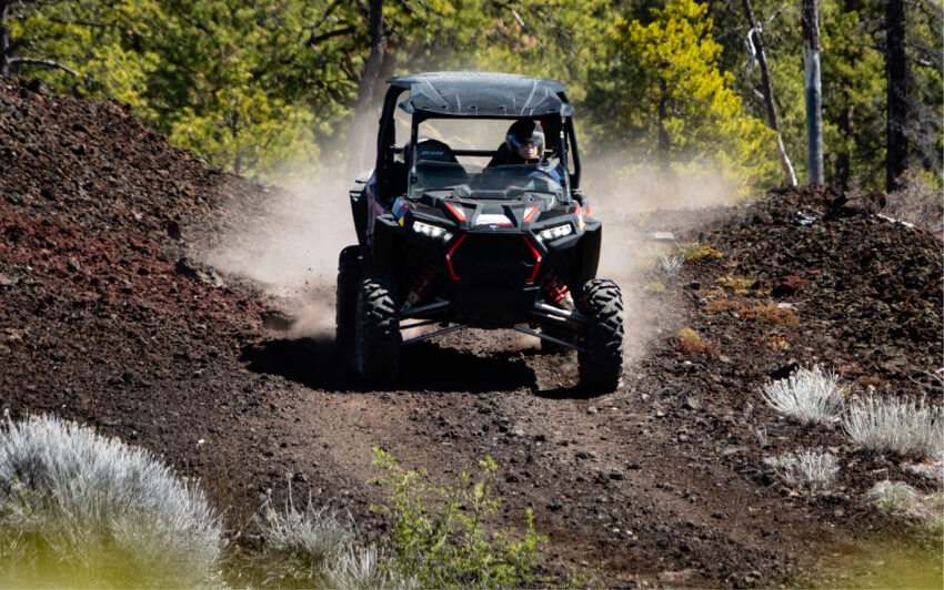 A person driving a UTV on a dusty dirt trail through a forest in Central Oregon.