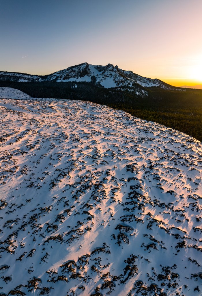 A snow-covered volcanic landscape at sunset with a mountain peak in the background in Central Oregon.