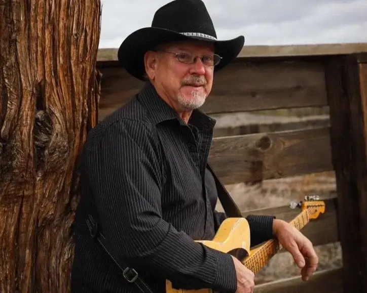 A man in a cowboy hat and black shirt holding an electric guitar in Central Oregon.