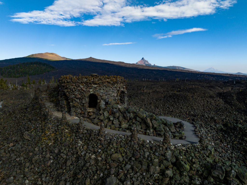 A stone observatory structure sits amidst a vast, rugged volcanic lava field in Central Oregon.