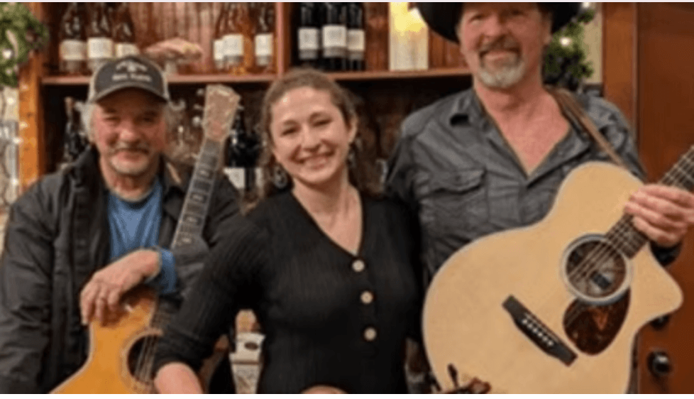 Three musicians posing together with acoustic guitars in front of a wine shelf in Central Oregon.