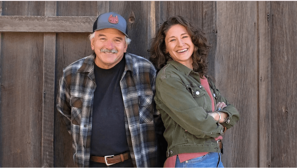 An older man and a younger woman smiling while leaning against a wooden wall in Central Oregon.
