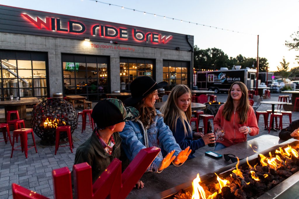 A group of people warming their hands by a fire pit at a brewery in Central Oregon.