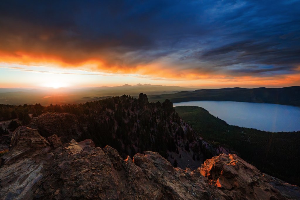 A dramatic sunset over a mountain lake with rocky foreground cliffs in Central Oregon.