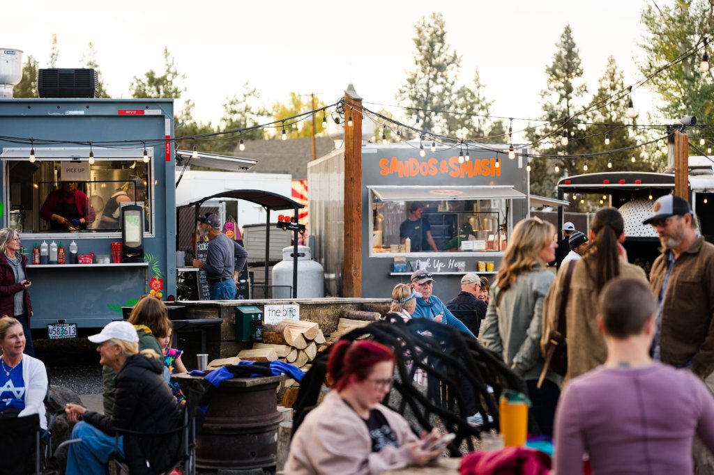 People gather at an outdoor food truck park with string lights overhead in Central Oregon.