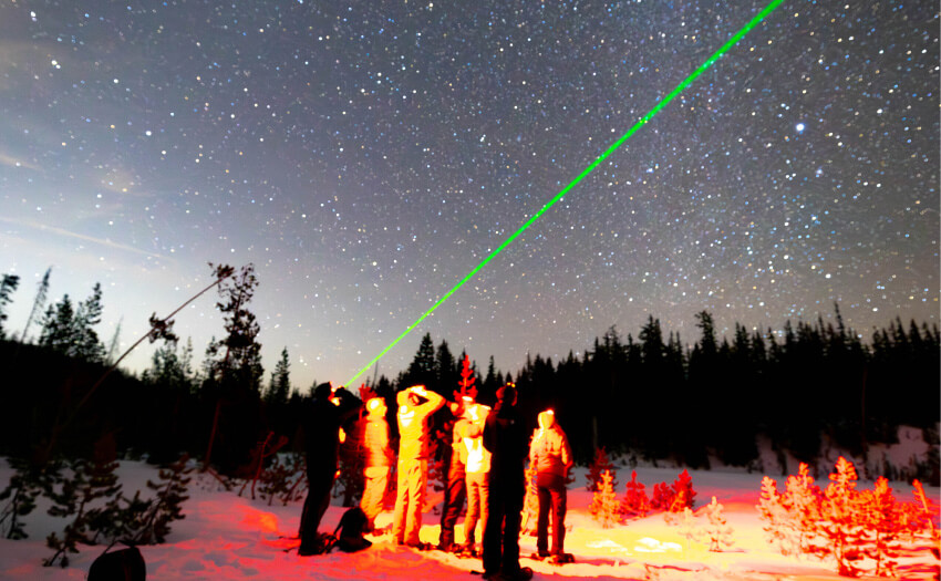 A group of people standing in snow pointing a green laser at the night sky in Central Oregon.