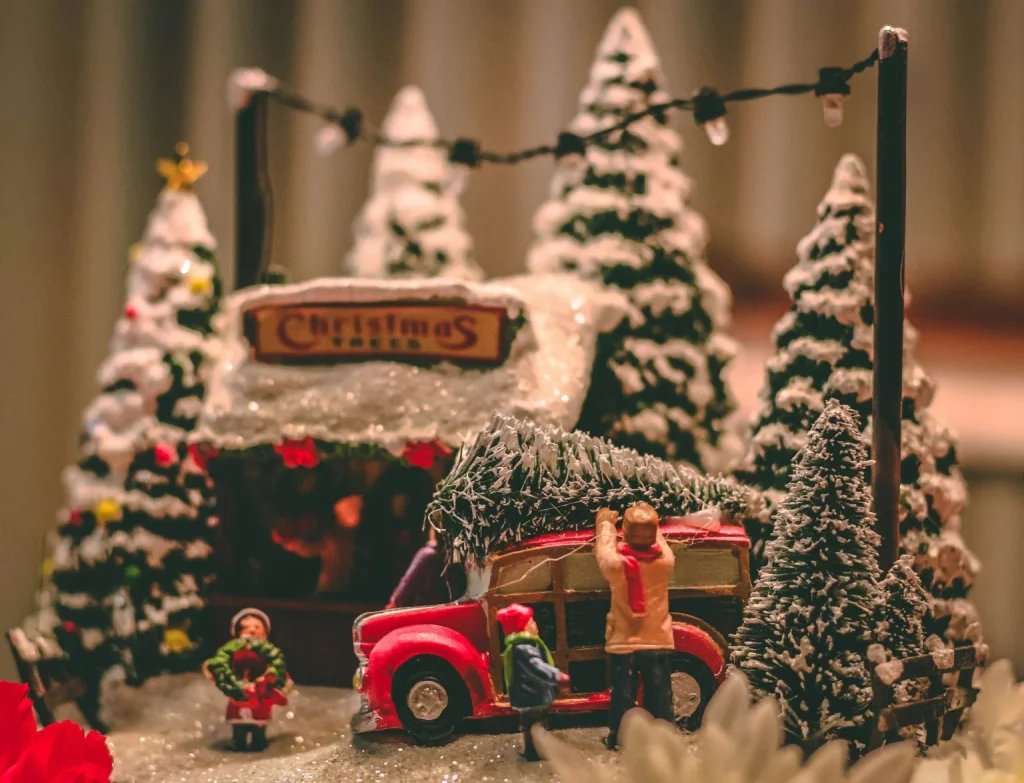 A miniature Christmas village scene featuring a red car carrying a tree in Central Oregon.