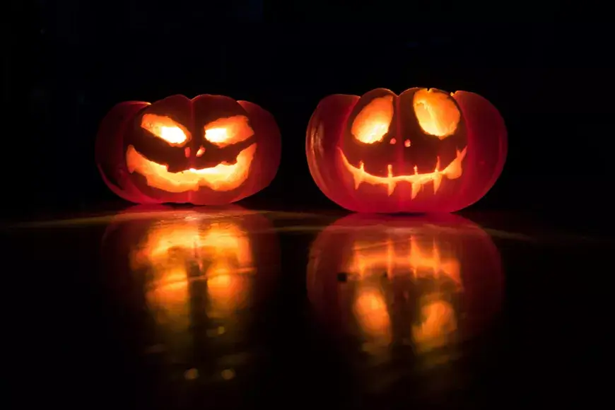 Two glowing jack-o'-lanterns with carved faces sit in the dark with reflections in Central Oregon.