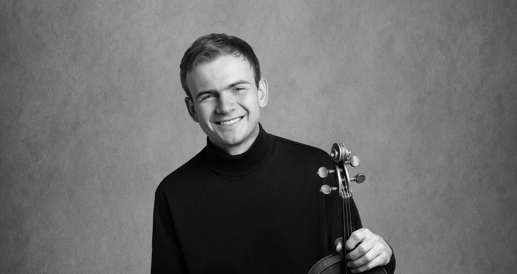 A smiling young man in a black turtleneck holding a violin in Central Oregon.