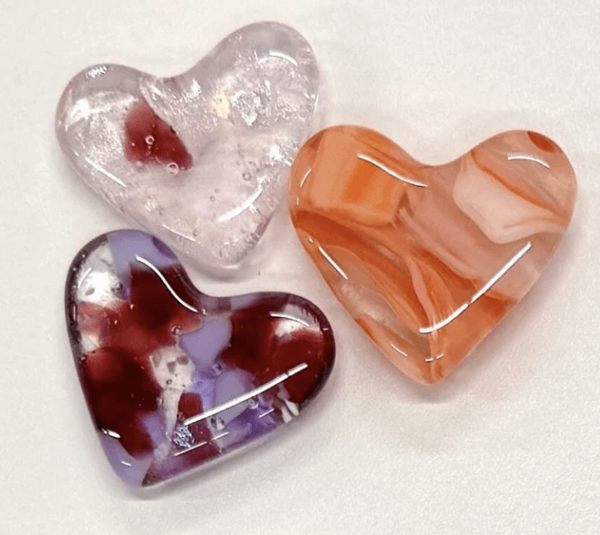 Three decorative glass hearts in clear, orange, and purple colors on a white background in Central Oregon.