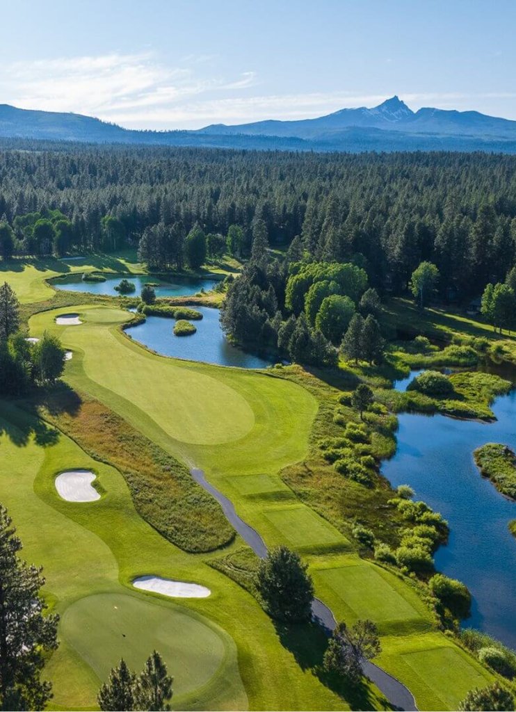 An aerial view of a scenic golf course surrounded by forest and mountains in Central Oregon.