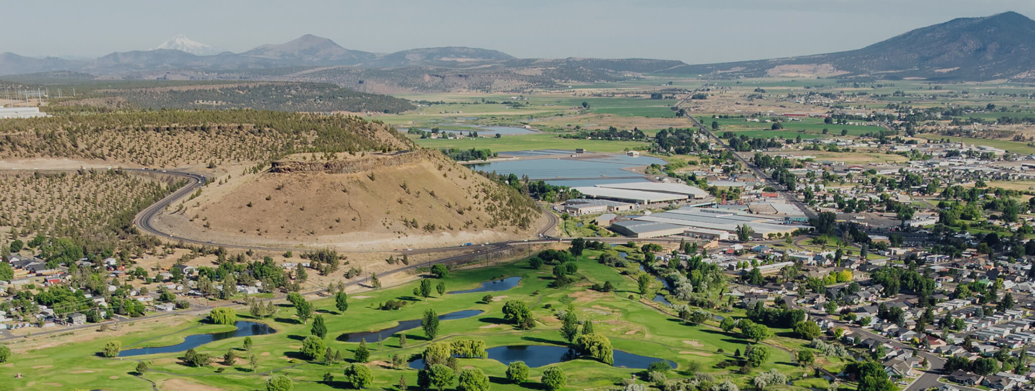 An aerial view of a golf course, a small town, and a large hill in Central Oregon.