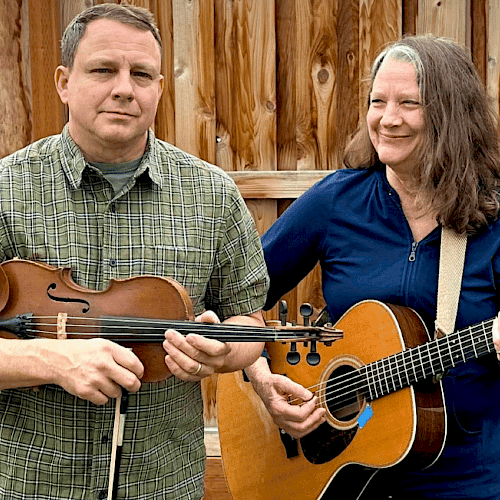 A man holding a violin and a woman playing an acoustic guitar in Central Oregon.