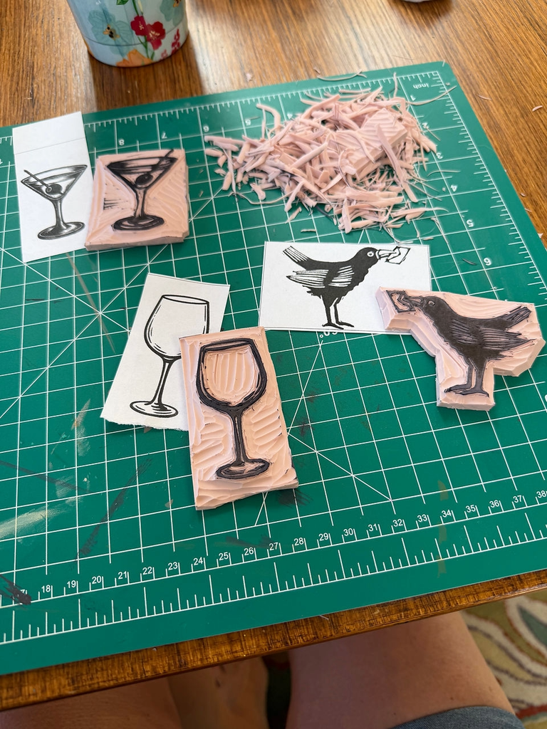 Linocut stamps of a martini glass, wine glass, and crow on a cutting mat in Central Oregon.