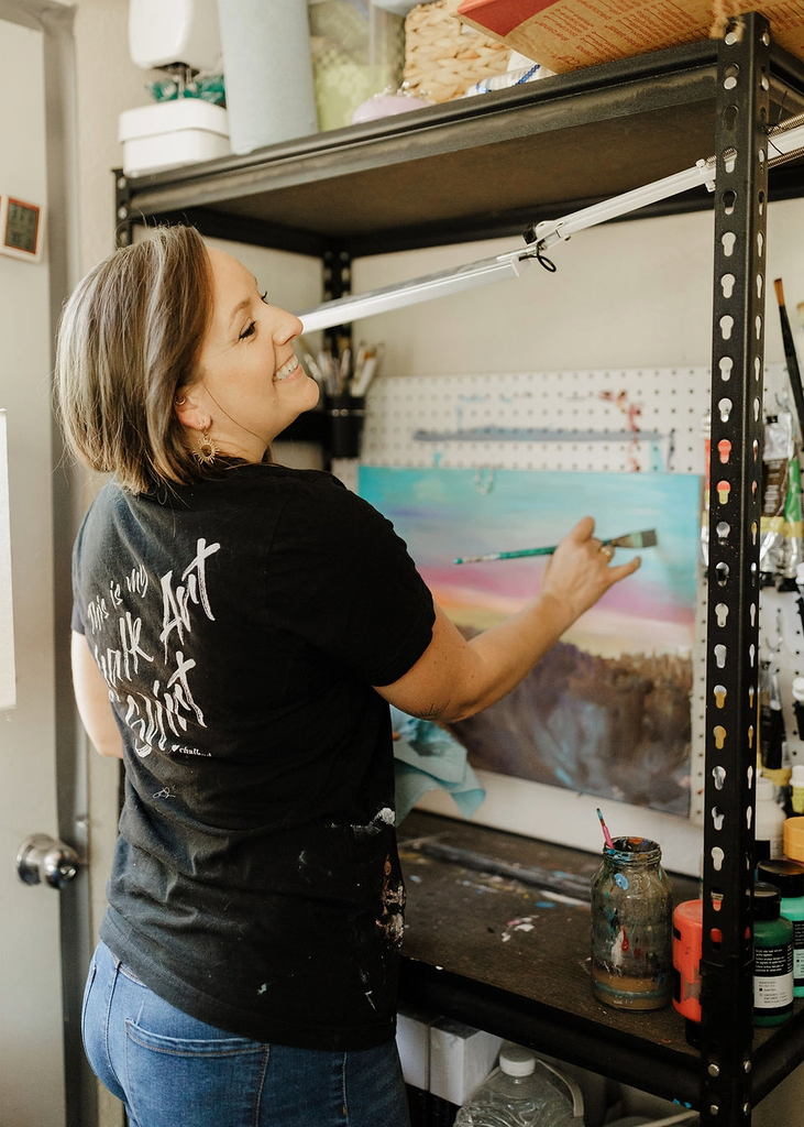 A smiling woman paints on a canvas in her art studio in Central Oregon.
