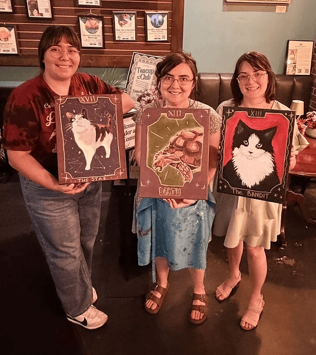 Three women holding their custom tarot-style paintings of animals in an art studio in Central Oregon.