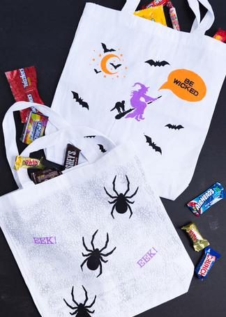 Two white Halloween tote bags decorated with spooky designs and filled with assorted candy in Central Oregon.