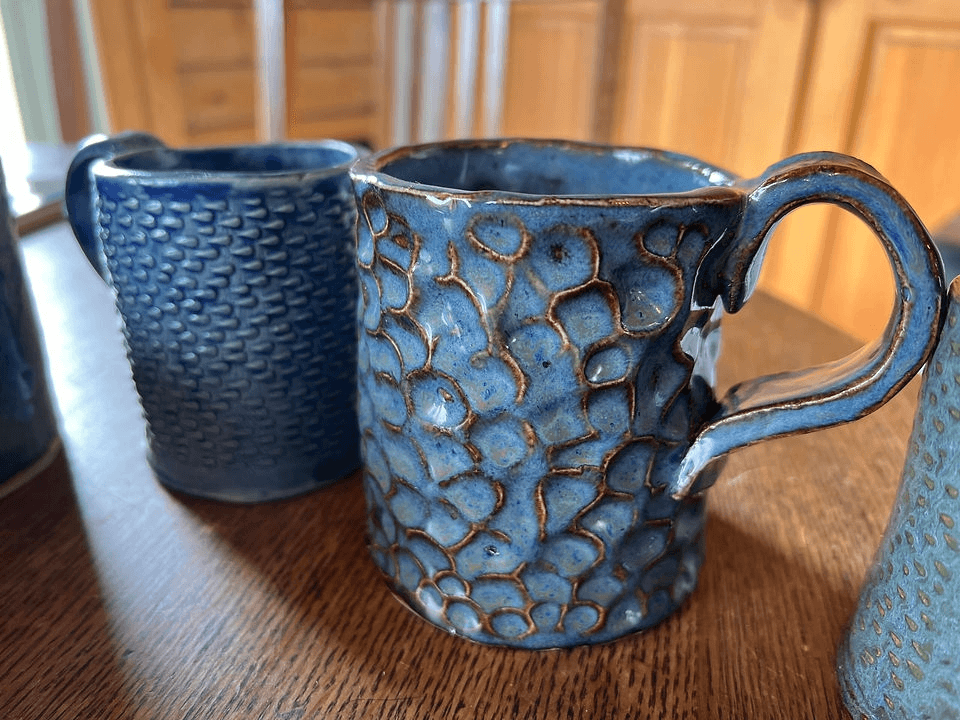 Two handmade blue ceramic mugs with textured surfaces sitting on a wooden table in Central Oregon.