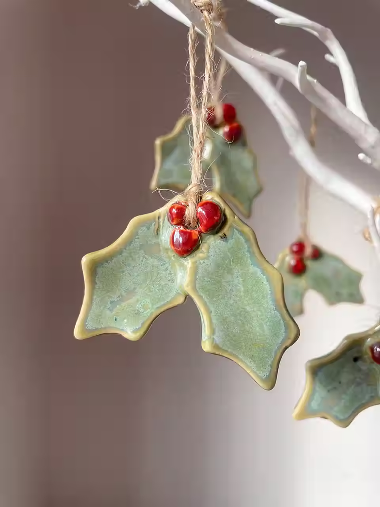 Ceramic holly leaf ornaments with red berries hanging from a white decorative branch in Central Oregon.