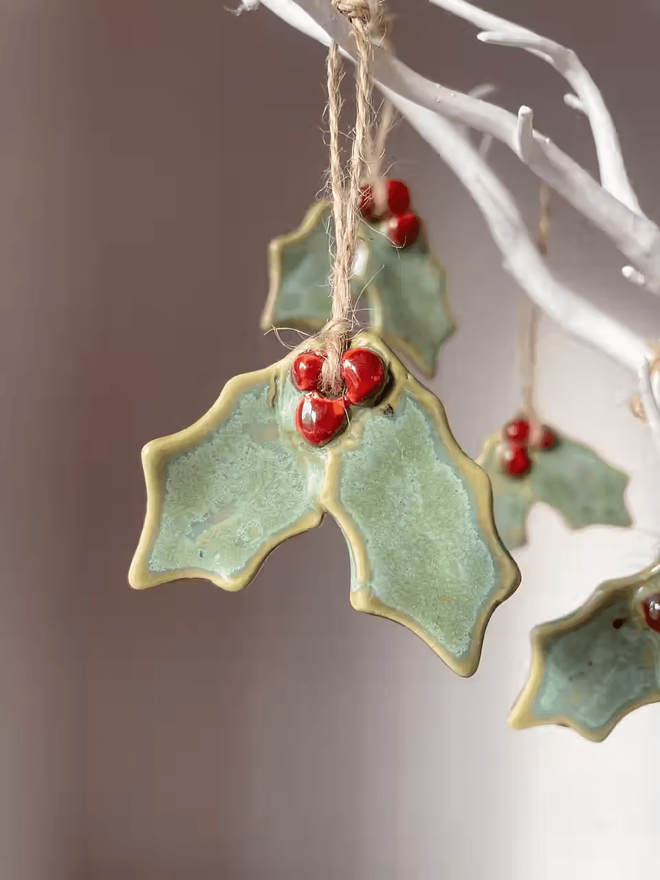 Ceramic holly leaf ornaments with red berries hanging from a white decorative branch in Central Oregon.
