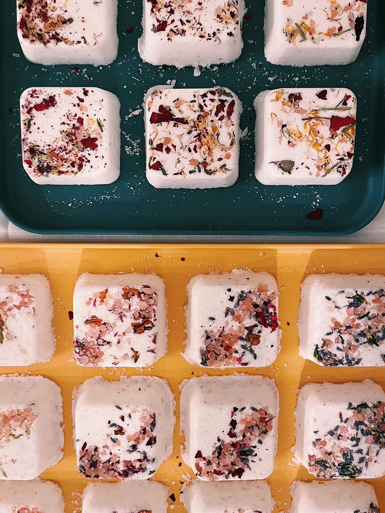 Rows of square bath bombs topped with dried flower petals on colorful trays in Central Oregon.