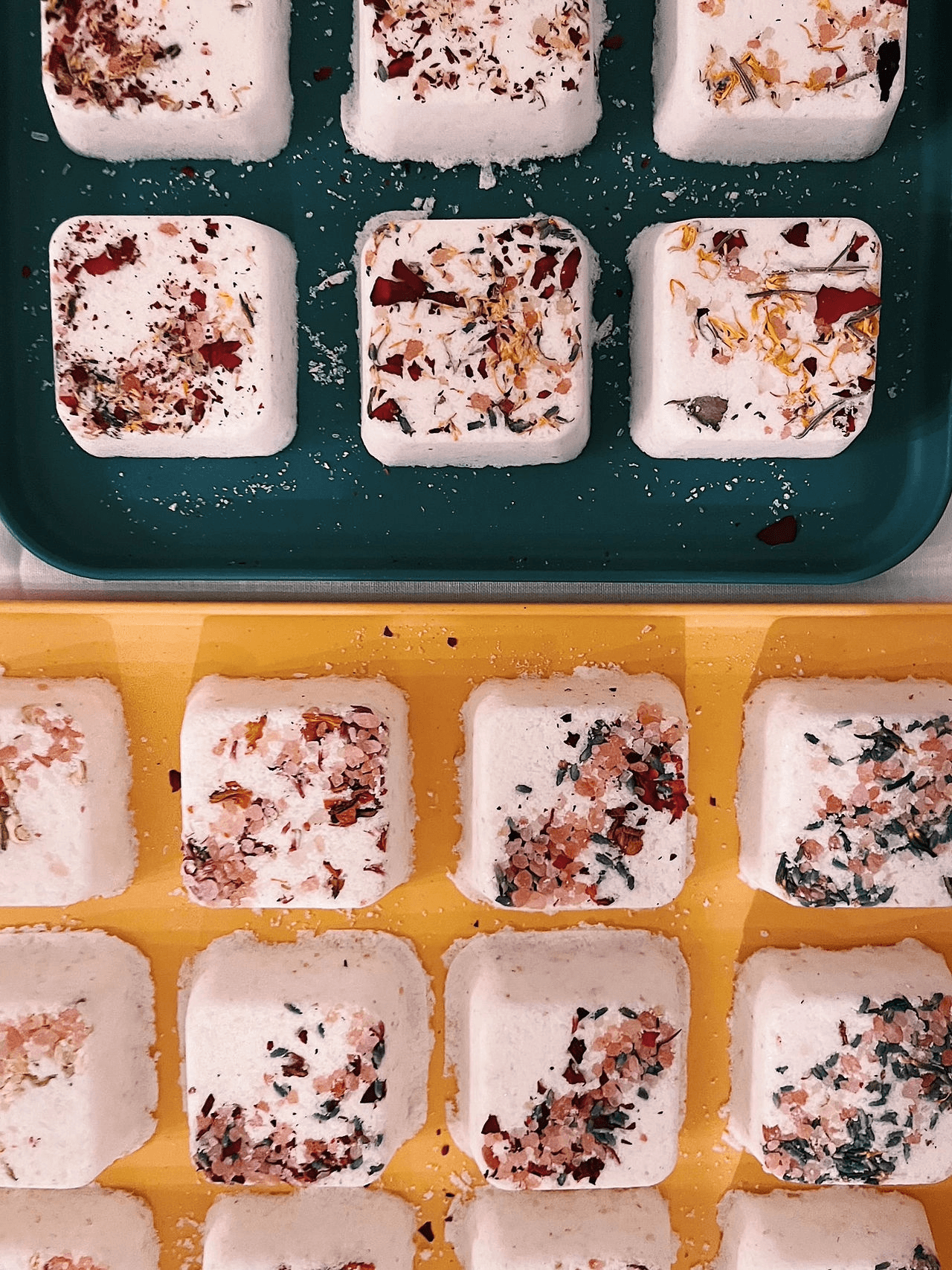Rows of square bath bombs topped with dried flower petals on colorful trays in Central Oregon.