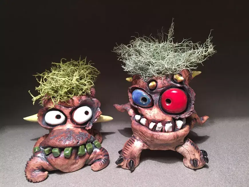 Two whimsical, textured clay monster sculptures with moss hair and large, colorful eyes in Central Oregon.