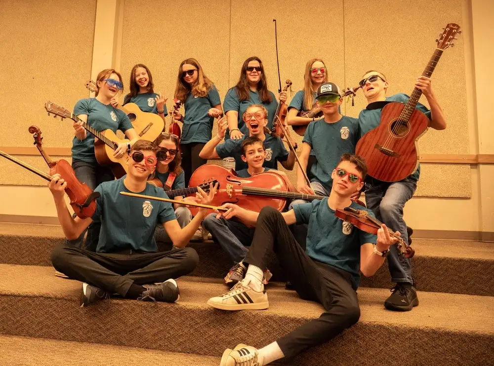 A group of teenagers in matching blue shirts posing with various musical instruments in Central Oregon.