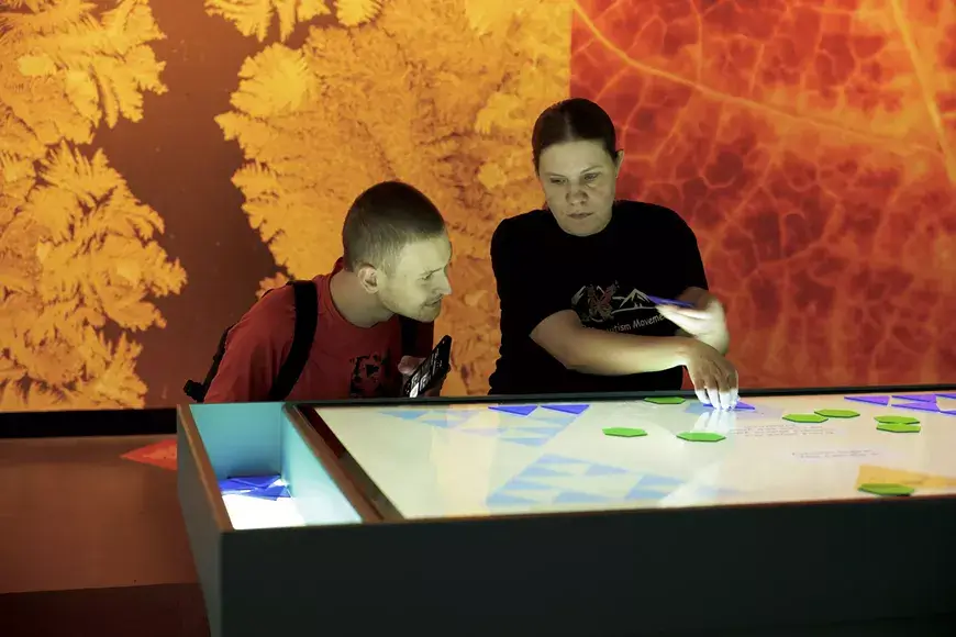Two people interact with an illuminated digital table display in a museum setting in Central Oregon.