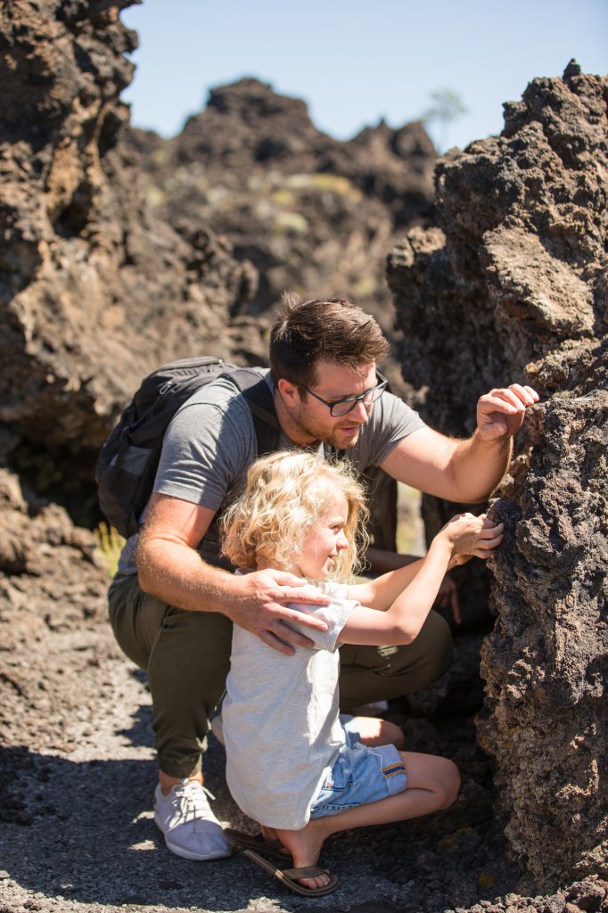 A father and child explore and touch rough volcanic rock formations outdoors in Central Oregon.