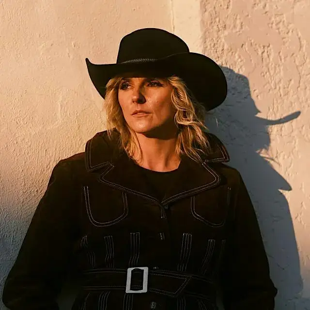 A blonde woman wearing a black cowboy hat and jacket against a textured wall in Central Oregon.