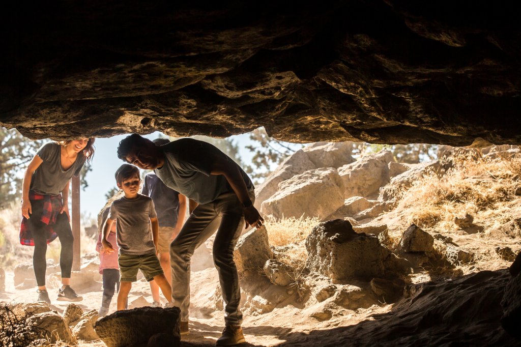A family explores the entrance of a rocky cave on a sunny day in Central Oregon.