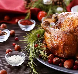 A roasted chicken garnished with pine branches, cranberries, and nuts on a wooden table in Central Oregon.