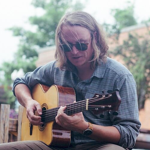 A man with long blonde hair and sunglasses playing an acoustic guitar outdoors in Central Oregon.