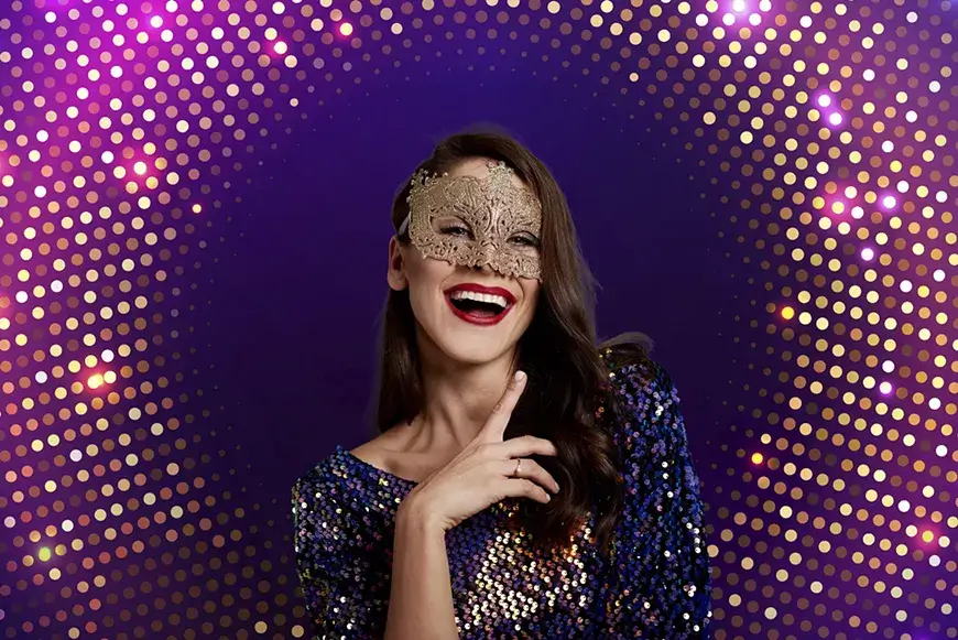 A smiling woman wearing a gold lace mask against a purple bokeh background in Central Oregon.